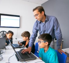 Pupils doing task on laptops and focused teacher monitoring them. Cute children sitting at table, using computers during lesson and studying at school. Knowledge and digital education concept